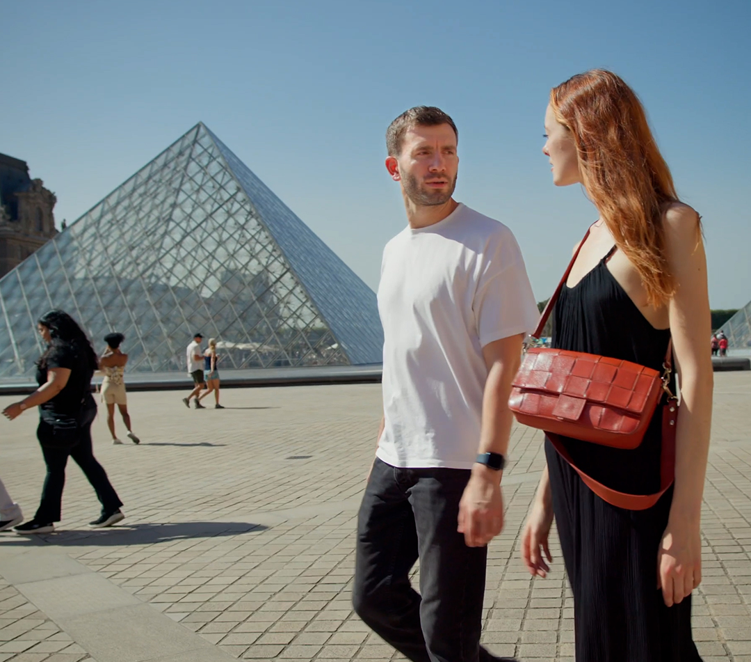 A young couple walks in front of the pyramid at the Louvre Museum
